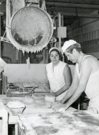 Bakery in Dolní Benešov in the 1970s, still as a functioning national enterprise of the Opava plant. In the background, a lifted dump dumped the dough onto a mat, the woman in the photo weighed it and prepared it for the man next to her. The man rolled out a loaf and put it in a floured wrapper.